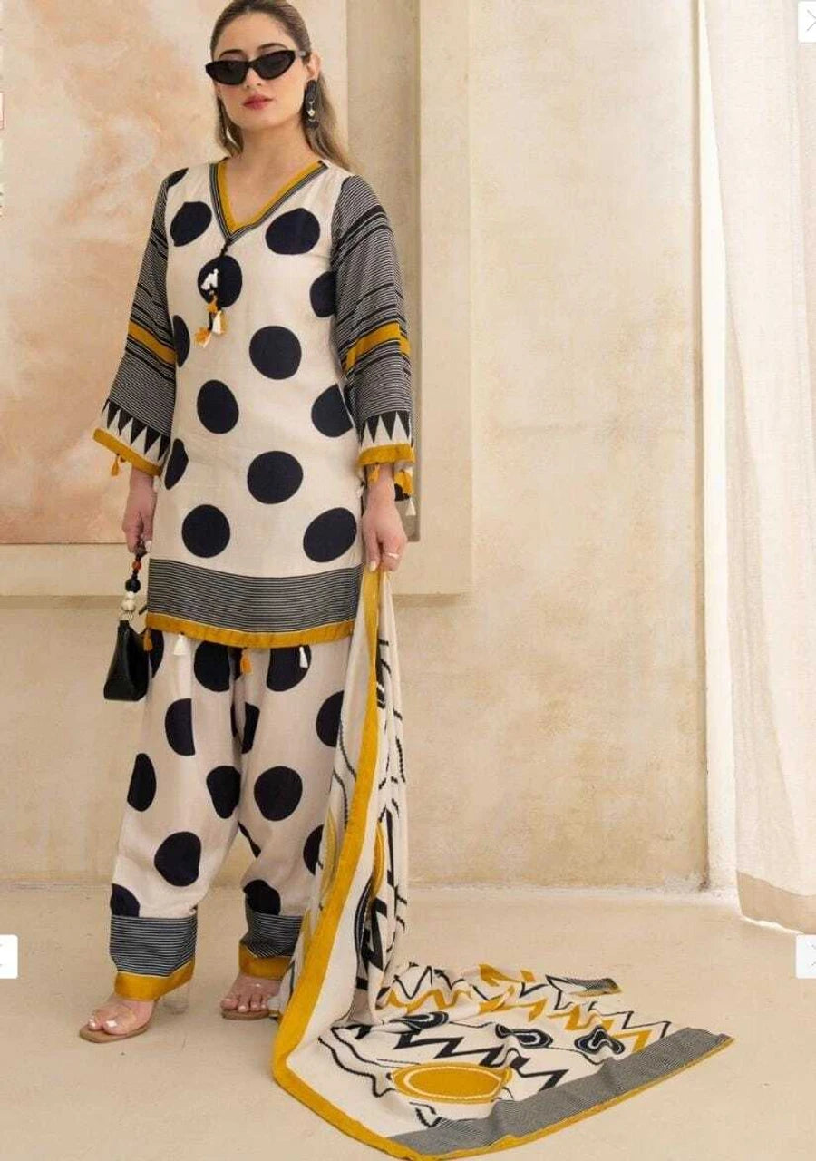 A woman models a three-piece traditional South Asian outfit with a cream kurta and pants featuring large black polka dots, gray sleeve panels, and mustard yellow accents, along with a matching dupatta.